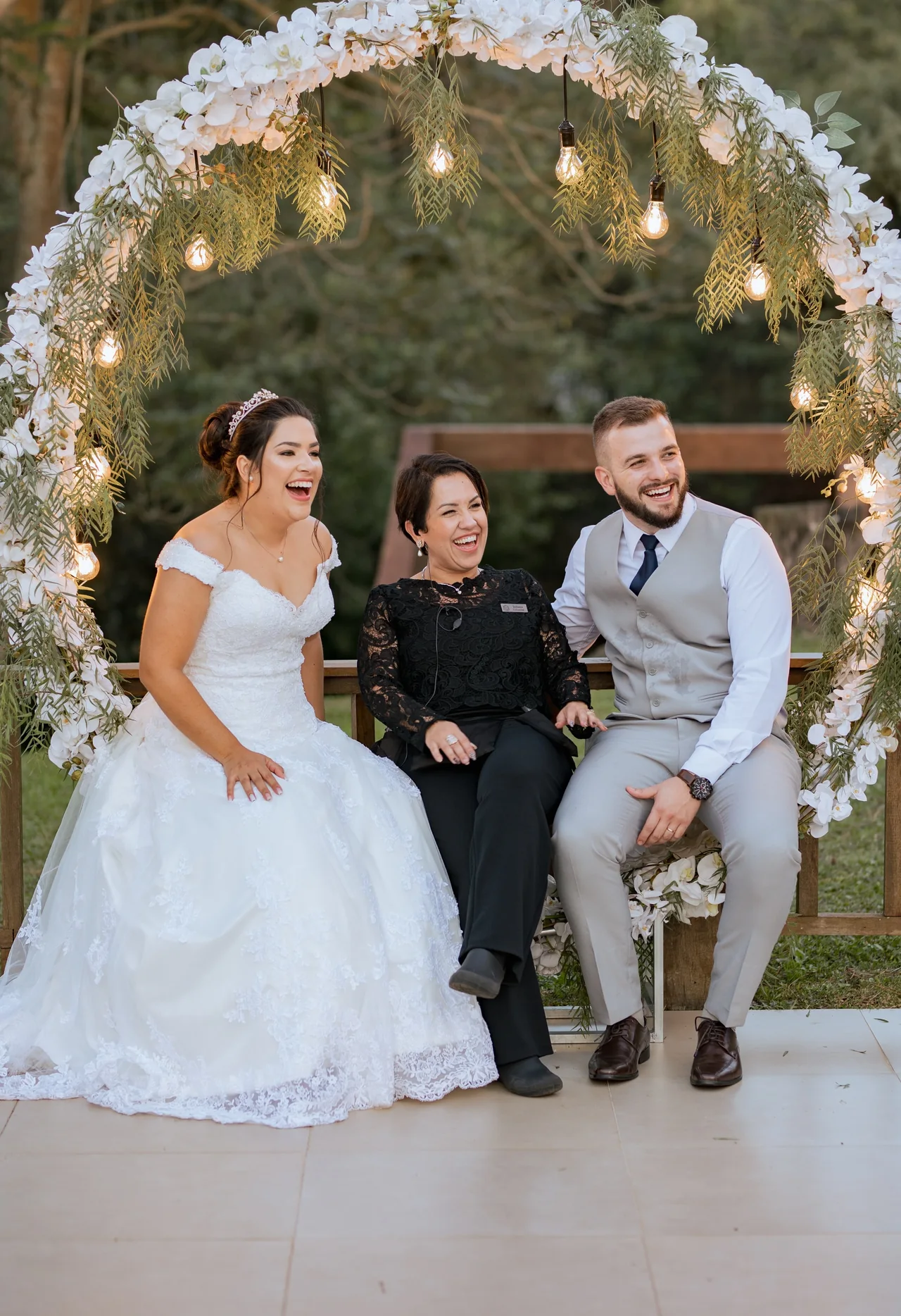 Juliana Porto sentada com um casal de noivos, todos sorrindo.