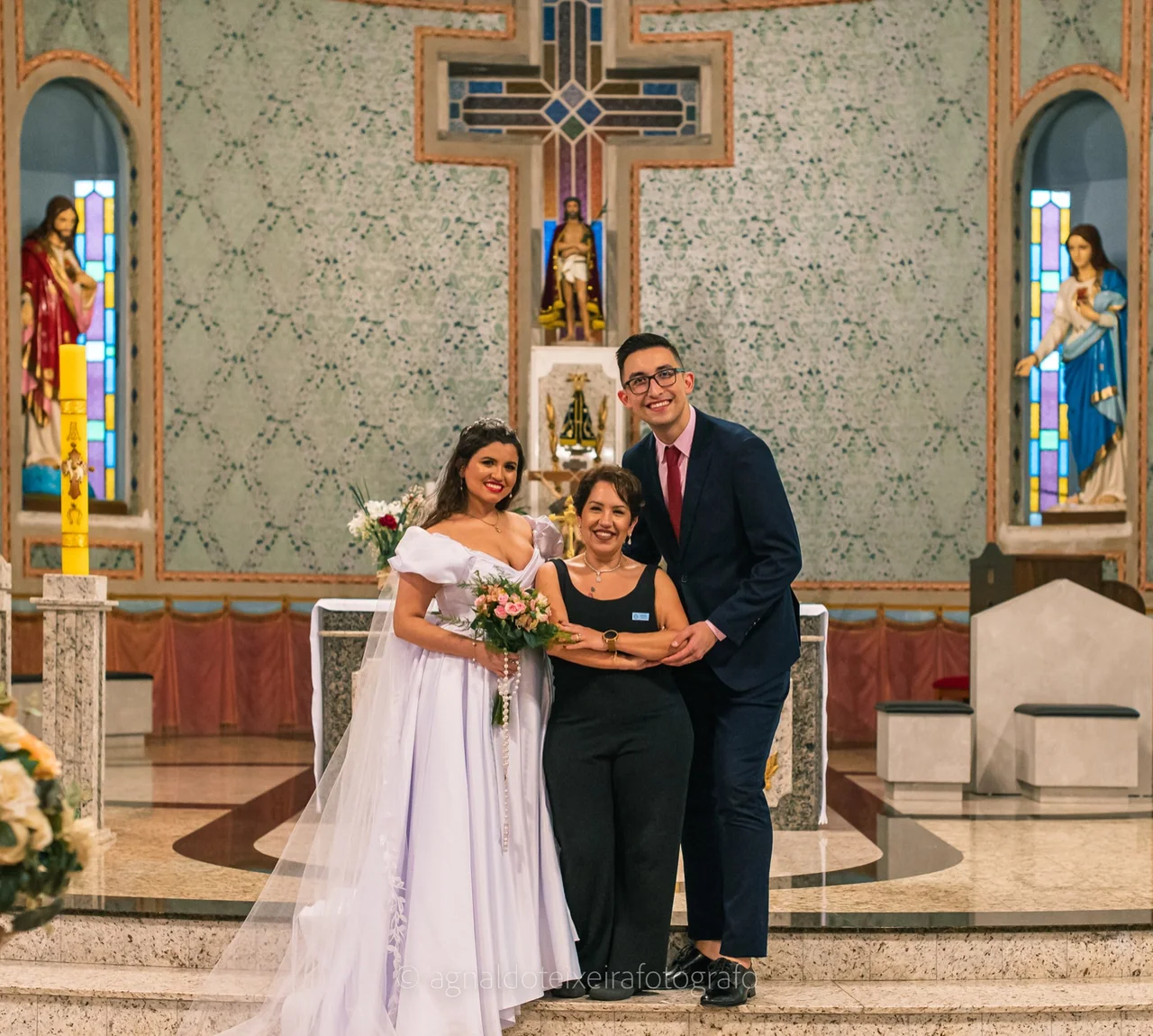 Juliana Porto abraçada aos noivos na igreja.