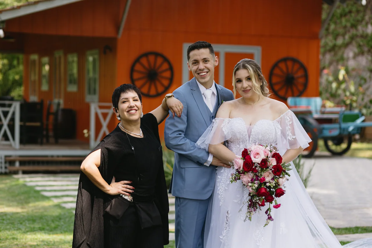Juliana Porto sorrindo ao lado dos noivos em um casamento ao ar livre.